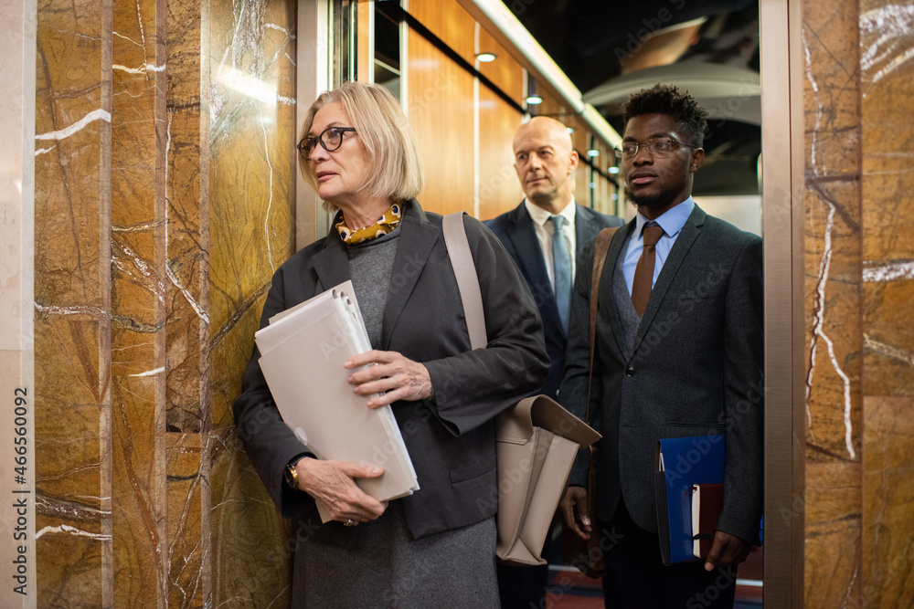 Poster group of contemporary intercultural co-workers with documents waiting for elevator while standing in