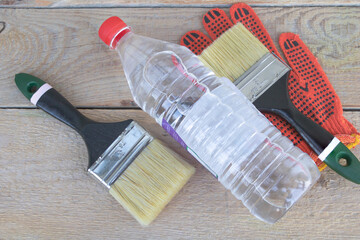 A bottle of acetone - two paintbrushes and gloves in the background - wooden background -...