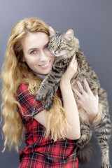 A joyful lady is holding a surprised tabby domestic cat in her arms. Love for cats