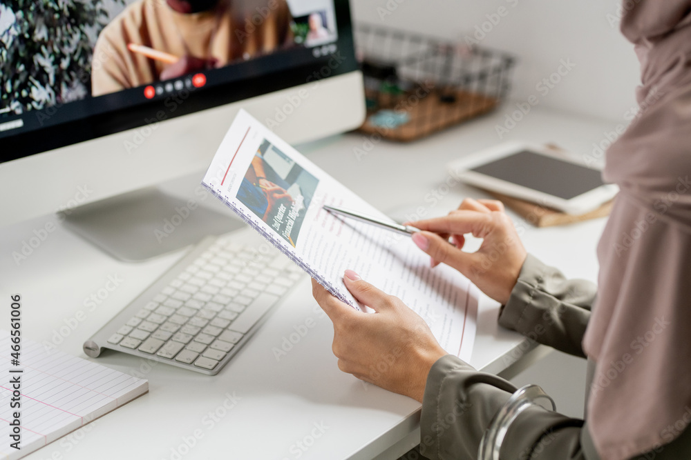Poster hands of young contemporary teacher pointing at document while sitting in front of computer with her