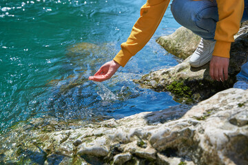 The girl collects crystal clear water from a mountain river in her palm