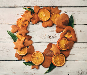 Christmas wreath from gingerbread cookies, baked orange slices, mandarine leaves on the white wooden table surface top view. Christmas evening still-life image.