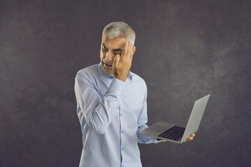 Shocking content. Frightened or shy senior businessman covering his eyes looking at laptop in his...