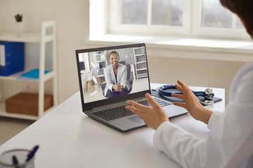 Online doctor sitting at table with laptop computer and stethoscope and counseling young female...