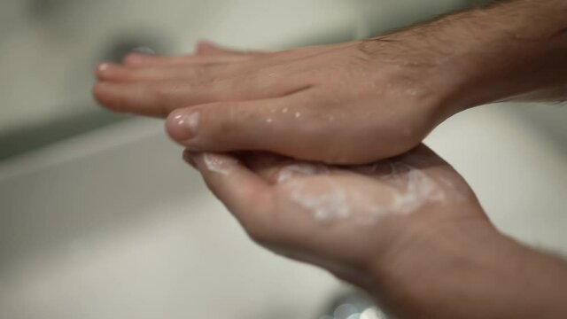 Close-up male hands rubbing shave foam in palms in slow motion. Unrecognizable young Caucasian man at home in bathroom shaving in the morning. Lifestyle and domestic routine concept
