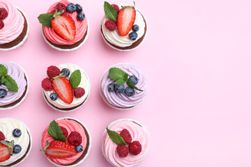 Different delicious cupcakes with cream and berries on pink background, flat lay. Space for text