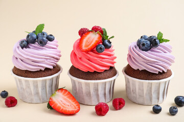 Different delicious cupcakes with cream and berries on beige background