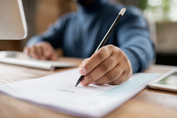 Hand of man holding pencil over document while sitting in front of computer and making notes during online lesson