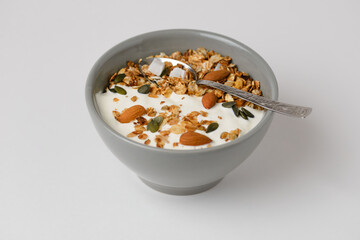 Traditional homemade breakfast granola with almonds, pumpkin seeds, coconut, dried oat flakes and other cereals with yogurt in a gray bowl with a spoon