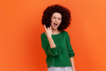 Excited enthusiastic woman with Afro hairstyle wearing green casual style sweater showing rock and...