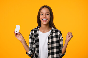Happy excited like a winner girl teenager student schoolkid holding credit card, laughing, winning a lot of money. Billionaire isolated in yellow background
