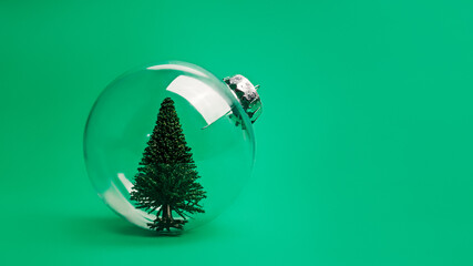 Creative Christmas composition with transparent glass ornament with pine tree inside on vivid green background. Minimal Xmas or New Year celebration concept. Minimal winter holidays idea. Copy space.