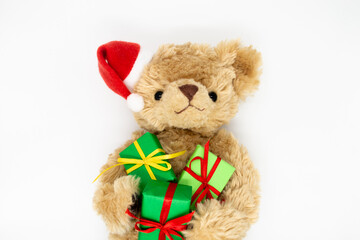 A stuffed toy Teddy bear in a red Santa Claus hat with a pompom on one ear, holding green gift boxes in its paws. White background, copy space. The concept of Christmas gifts, sales