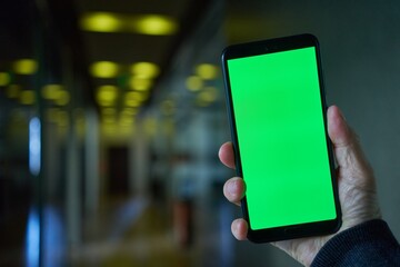 Hand holding mobile phone with chromakey green screen in modern office, walking, moving.