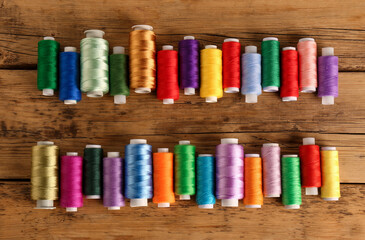 Different colorful sewing threads on wooden background, flat lay