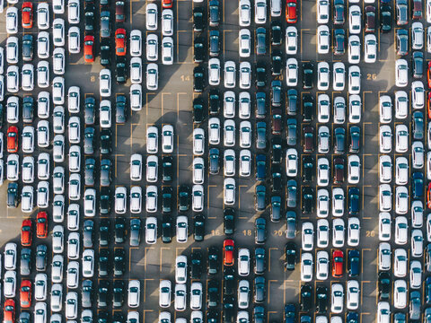 New multi-colored passenger cars stand in straight rows on a giant paved marked parking lot on the territory of an automobile manufacturing plant, overproduction