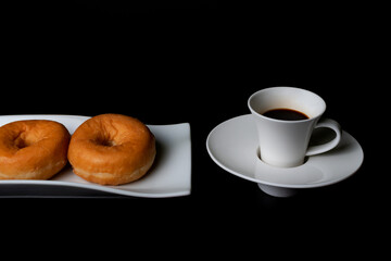 Breakfast or snack of a cup of coffee and some glazed donuts on a black background.