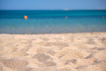 Close up of clean yellow sand surface covering seaside beach with blue sea water on background. Travel and vacations concept