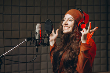 Young woman in headphones emotionally singing in microphone in the sound recording studio. Star,...