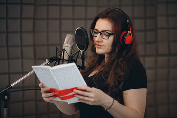 Professional female voice artist with headphones talking on mic during dubbing or voiceover. Online radio and podcasting concept.