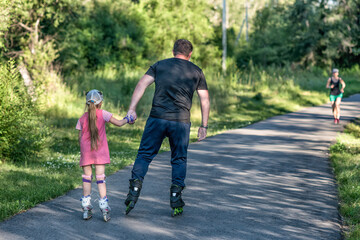 A father teaching his daughter roller skating in a park on summer day. Happy week-end. Father's day.