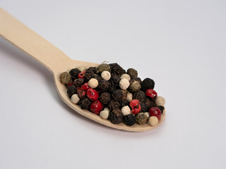 colored pepper in grains on a wooden spoon spice used in the kitchen, lot of detail macro photo, white background, eco concept