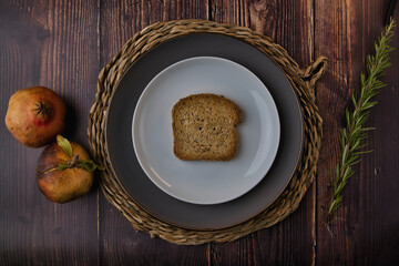 Scene of toasted bread cut in half with white plate and old wood background, and fresh rosemary branches.