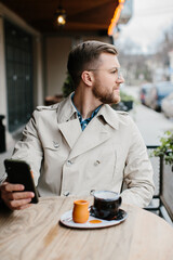 Young man drinking coffee and talking on the phone in an outdoor cafe.