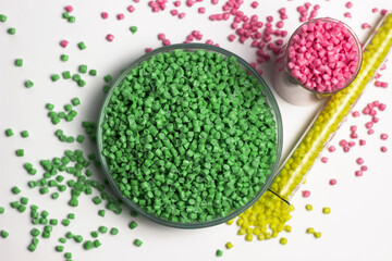 Green, yellow and pink  granules of polypropylene or polyamide on a white background. Plastics and polymers industry. Copy space. Glass petri dish, flask, volumetric glassware, test tube. 