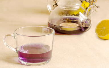 purple tea in a glass mug, a teapot with lemon in the background