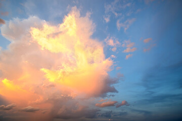Dramatic sunset landscape with puffy clouds lit by orange setting sun and blue sky.