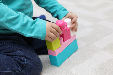 Little child playing with building blocks on carpet, closeup