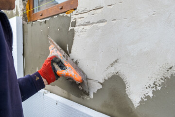 Construction worker covering house wall with adhesive cement glue berore installing styrofoam...