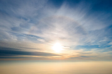 Aerial view of bright yellow sunset over white dense clouds with blue sky overhead.