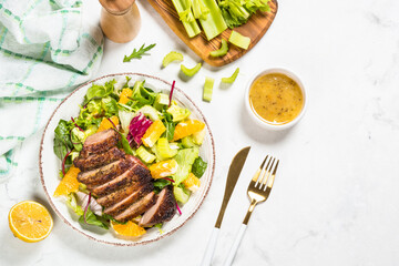 Salad with baked duck, green salad mix and oranges and honey mustard dressing. Healthy food, diet meal. Top view at white marble table.