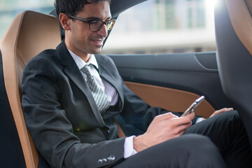 Businessman using his smartphone in a car's backseat