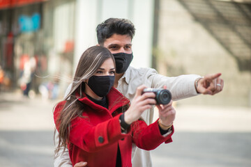 Happy tourists with covid or coronavirus masks couple whalking together in a city and photographing