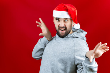 Fototapeta premium a bearded man in a red Santa Claus hat grins and makes various poses with his hands.