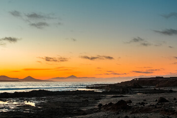 Obraz premium Dusk silhouette view on volcano Teide on Tenerife (right) and volcano Galdar on Gran Canaria from El Confital Beach in La Isleta, Las Palmas de Gran Canaria, Canary Islands, Spain. Iconic seascape.