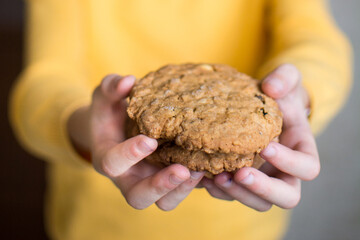 Biscuits with oats in the girls small hands, which has a yellow sweater and braids