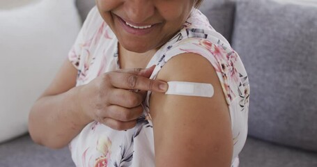 Smiling african american senior woman showing bandage on arm after covid vaccination - Powered by Adobe