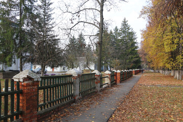 Autumn landscape. Walking path along the stone fence. Fallen leaves on the ground.