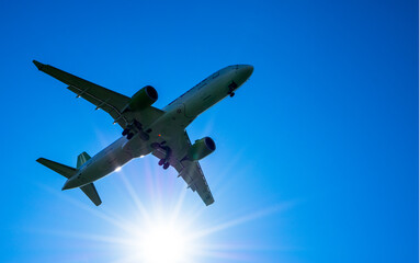 An airplane in the blue sky with the direct sun in the background. Bright sun and sunlight.