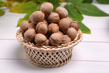Wicker bowl of ripe walnuts on white wooden table