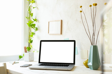 Stylish home office desk with laptop mock up, office supplies, frame, vase, green ivy and beige natural texture wall. Distance working and learning concept. Trendy, creative workspace.