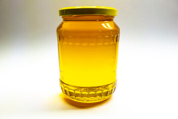 Fresh honey from bee plastic in a glass bottle with a cap on a light background.