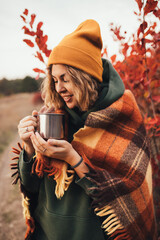 Young woman drinking hot tea from thermos in beautiful autumn forest.