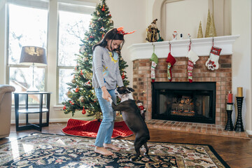 Girl dancing with her pet dog in front of Christmas tree and fireplace