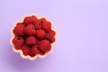 Bowl of fresh delicious raspberries on violet background, top view. Space for text