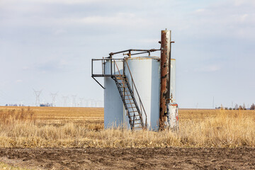Old oil well storage tanks in farm field. Oil well abandonment, environment pollution, and oil...